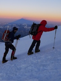 Climbers high on Elbrus with the mountain's shadow.