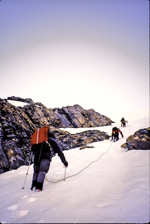 Climbers more up a steeper section of snow.