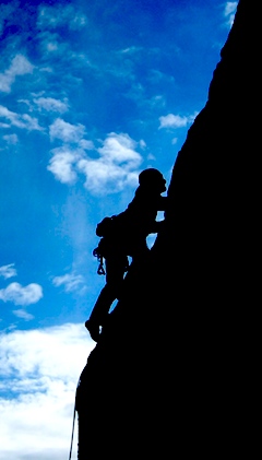 A lead climber silhouetted against a deep blue sky in Joshua Tree
