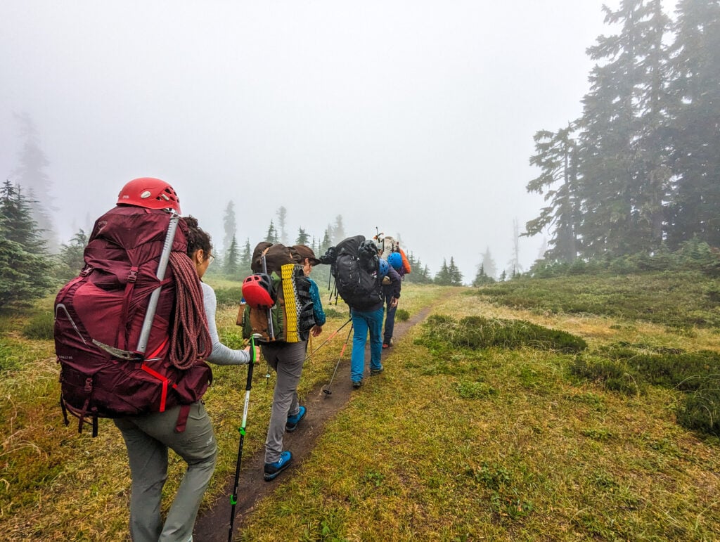 Hikers navigate through an alpine meadow in the dense fog on an AAI course