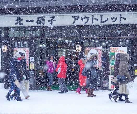 Japanese residents and tourists walking along a snowy street in front of a shop.