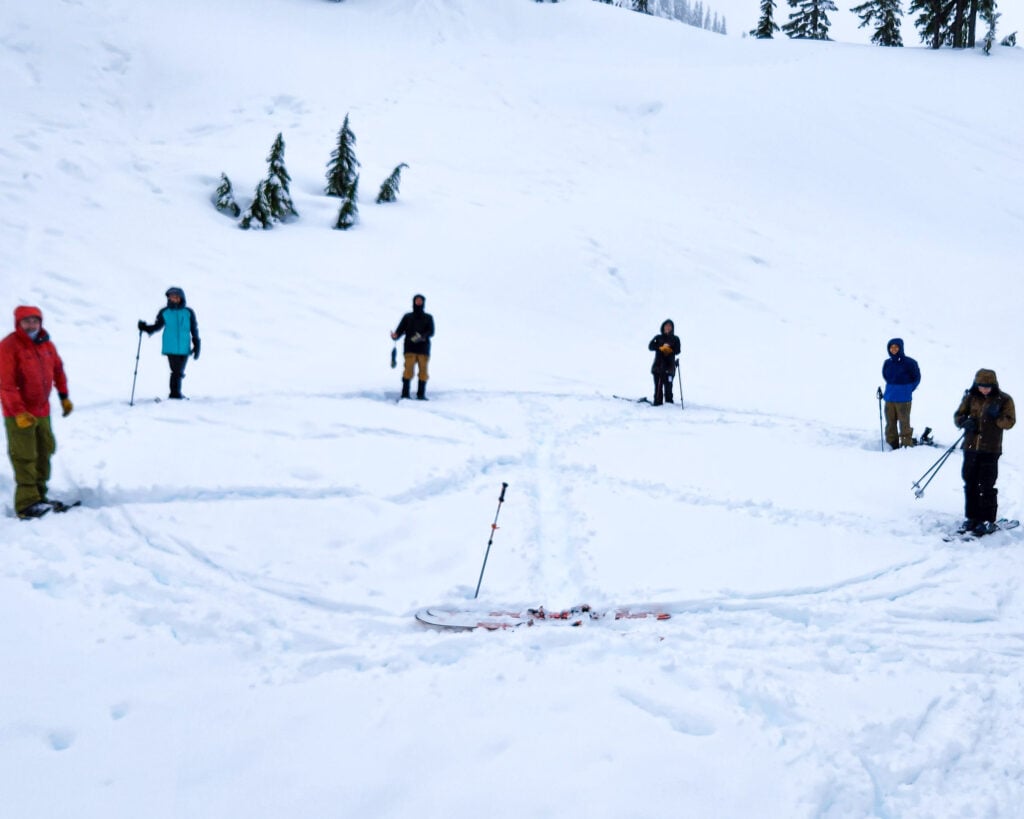 Students in a circle in the Mt. Baker backcountry do an avalanche beacon drill with the American Alpine Institute during their AIARE Rescue course