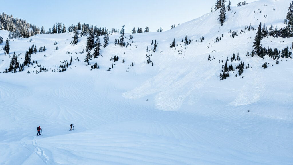 Two backcountry skiers look on at avalanche debris in the fresh snow of the Mt. Baker backcountry on their AIARE Avalanche course with the American Alpine Institute