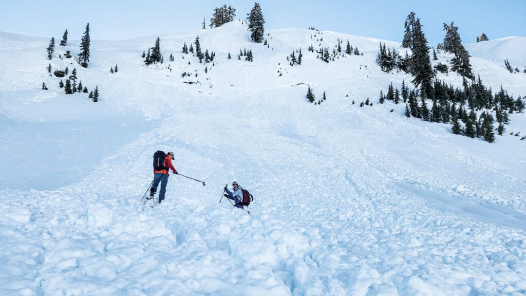 A backcountry skier offers their pole to help their partner out of avalanche debris in the Mt. Baker backcountry
