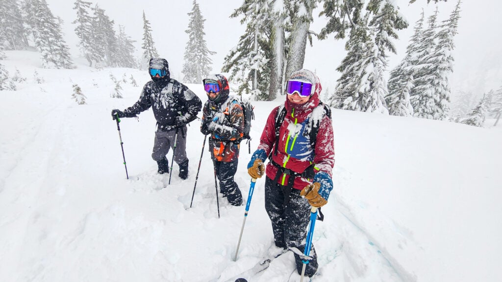 Three skiers stand in the woods during a snowy day