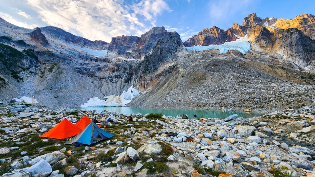 Tents set up next to an alpine lake surrounded by mountains and glaciers in the North Cascades