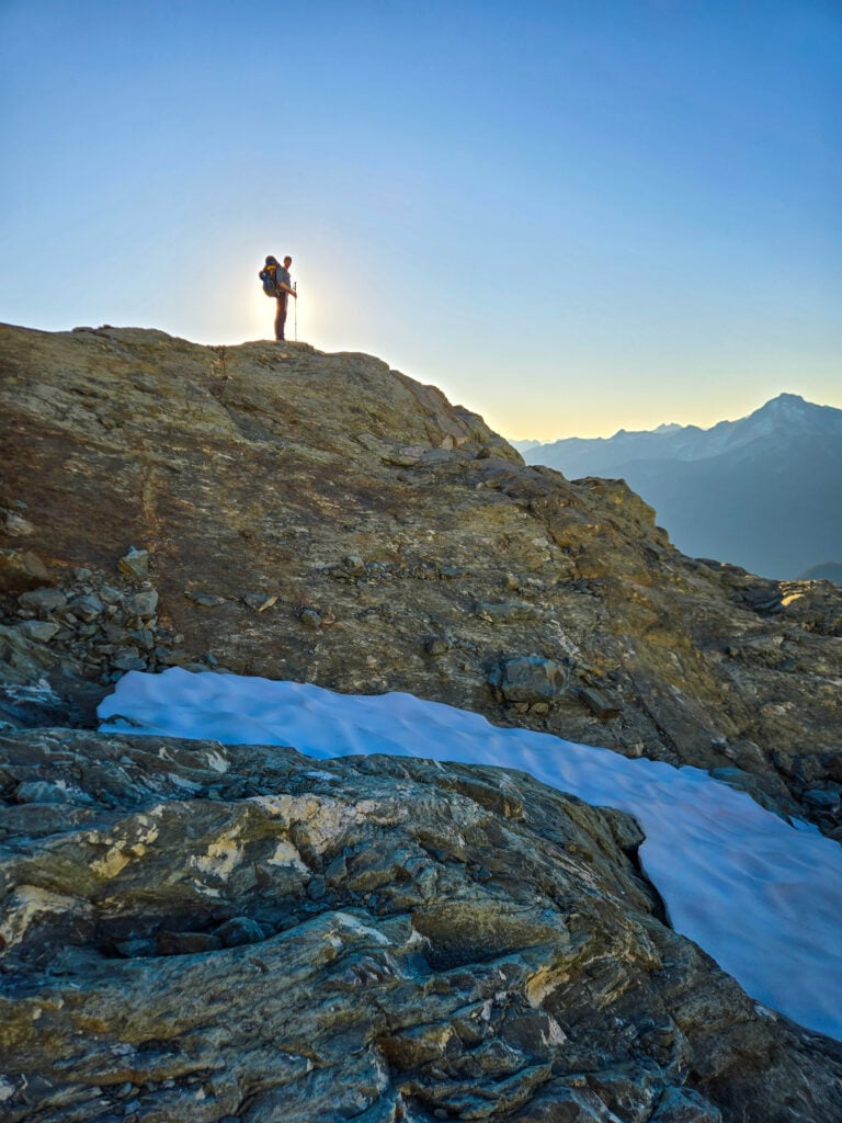 A lone backpacker backed by sunlight in the backcountry of the North Cascades