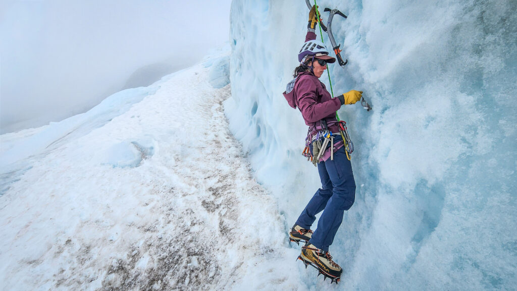 A student places an ice screw into the glacier ice to protect their progress up the serac.