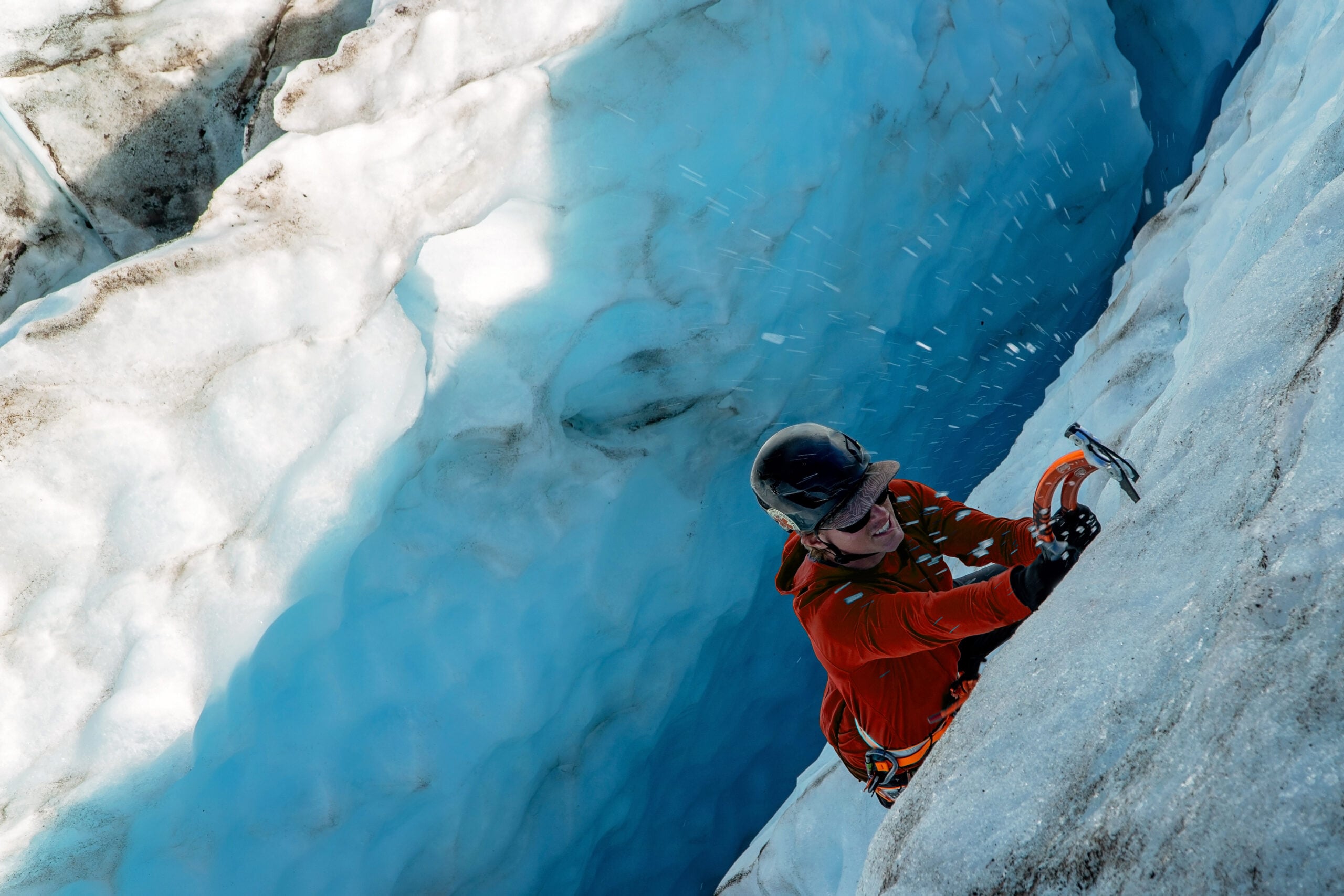 A climber on the Alpine Ice Introduction course swings their ice axe into blue alpine ice.