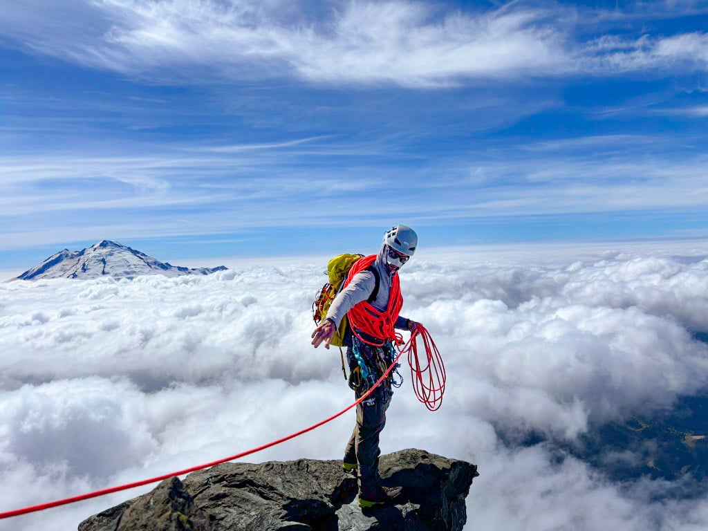 A climber manages the rope at the summit above the clouds on Mt. Shuksan during an American Alpine Institute mountaineering course