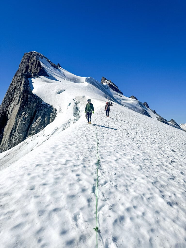 Students descend a narrow ridge of glacier in the remote alpine wilderness of the North Cascades during American Alpine Institute Alpine Mountaineering and Technical Leadership Part 4 (AMTL4)