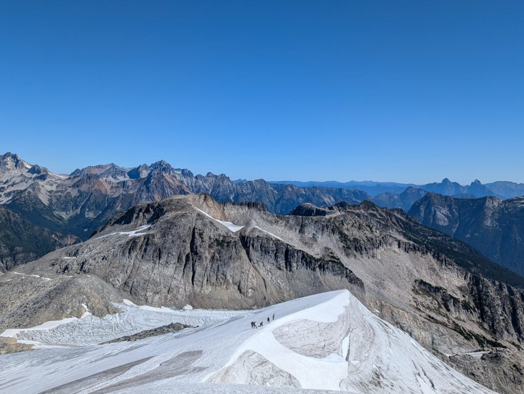 A rope team in the distance navigates a remote glacier in the alpine wilderness of the North Cascades during an American Alpine Institute Alpine Mountaineering and Technical Leadership Part 4 (AMTL 4)