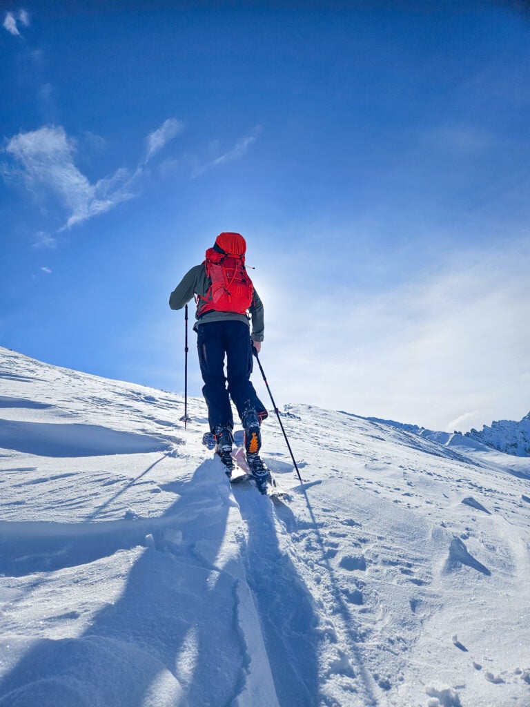 A skier makes their way up a slope while skinning to reach the peak before dropping back down, earning their turns on an American Alpine Institute ski course