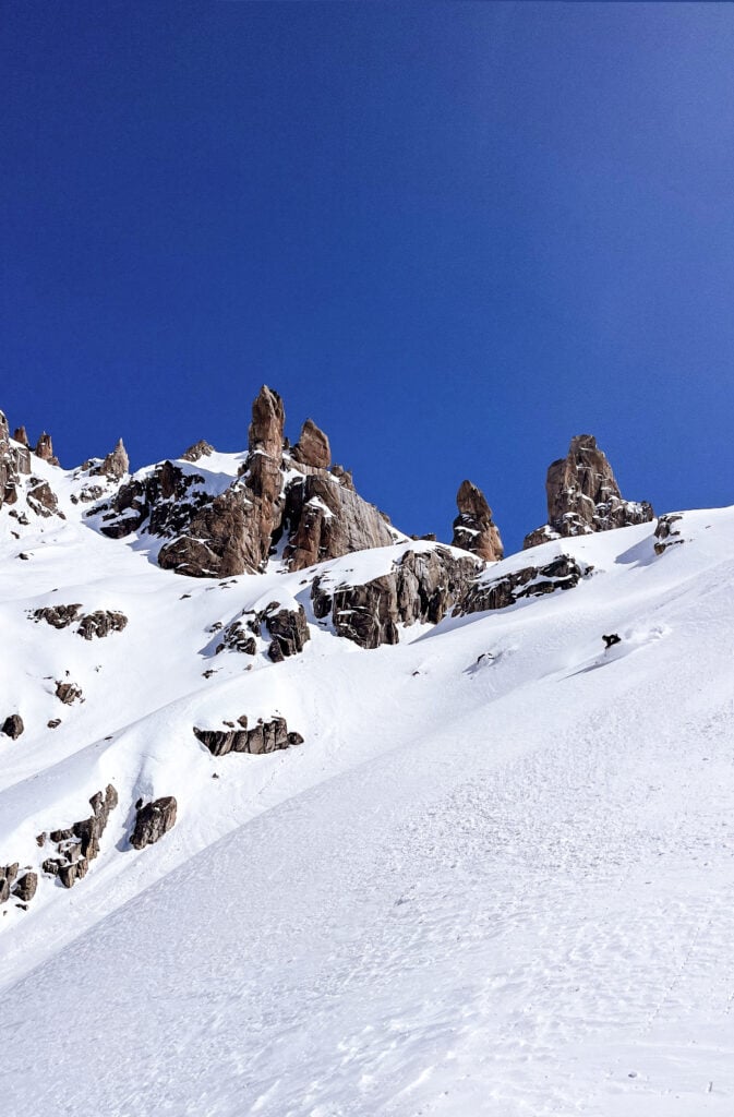 A skier makes a wave of snow as they descend a steep slope after reaching the peak in an American Alpine Institute ski course