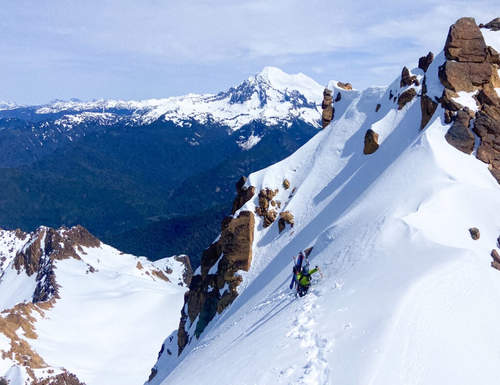 Skiers ascend a steep peak, earning some backcountry ski turns with Mt. Baker in the background on an American Alpine Institute Ski course