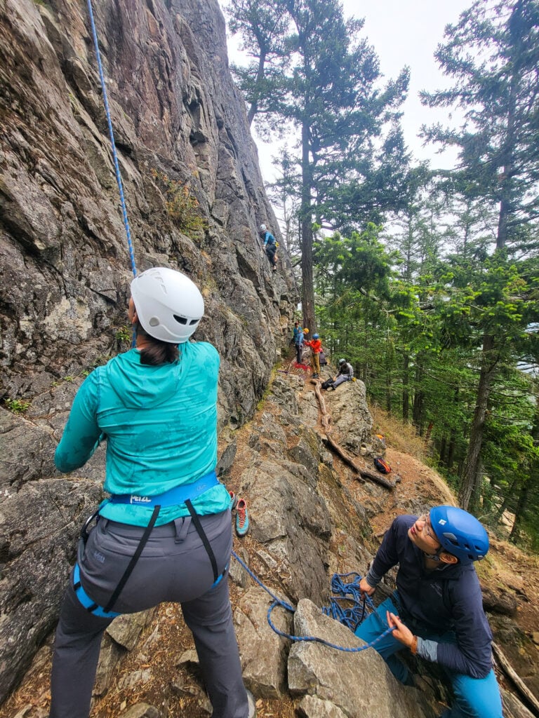 A class of climbers learn how to rock climb at Mt. Erie. Some belay while others learn movement on rock on an American Alpine Institute rock climbing course.
