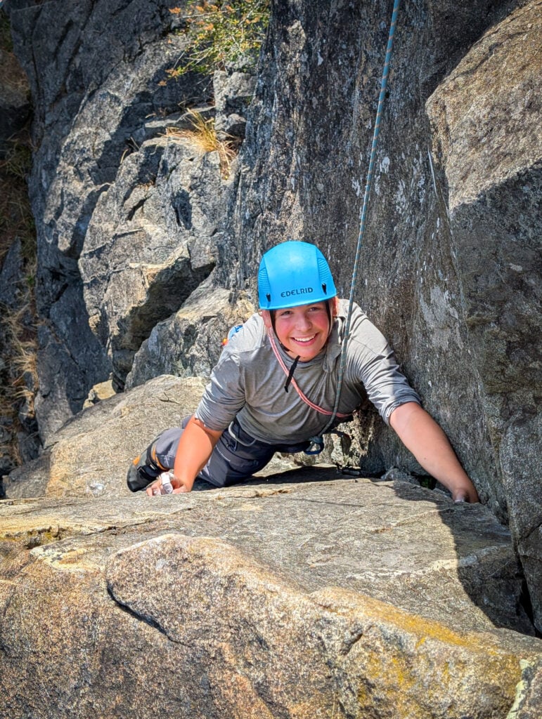 A student smiles as they near the top of the climbing route at Mt. Erie on an American Alpine Institute Leaders of Tomorrow Rock Climbing Camp
