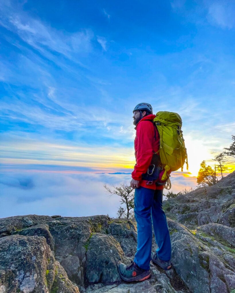 A rock climber looks out over the foggy Puget sound at the top of Mt. Erie during an American Alpine Institute rock climbing course