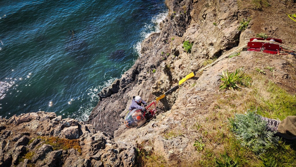 A student practices on a cliff face with a litter over the Puget Sound on an American Alpine Institute rope rescue program