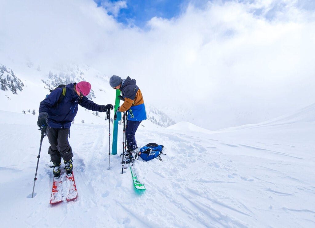 A pair of skiers transition from downhill to uphill mode putting on their skins and clipping in their boots on an American Alpine Institute Ski program in the Mt. Baker Backcountry