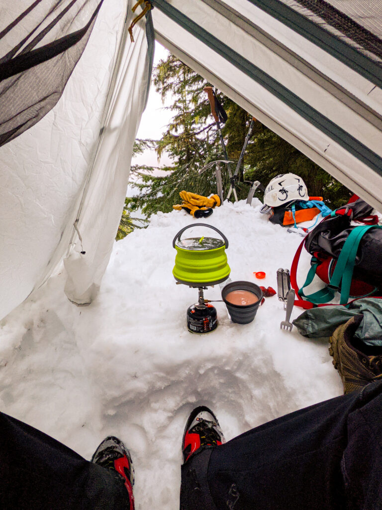A camper makes their dinner in their winter campsite on an American Alpine Institute winter camping course