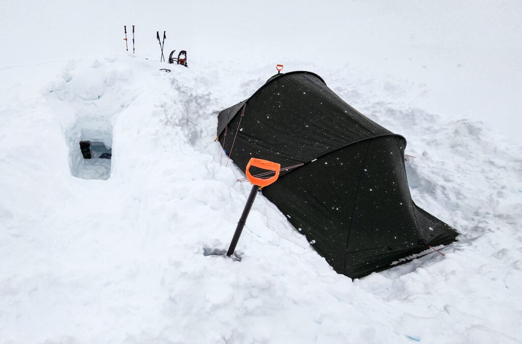 A snow cave next to a tent, set up during a winter camping course with the American Alpine Institute