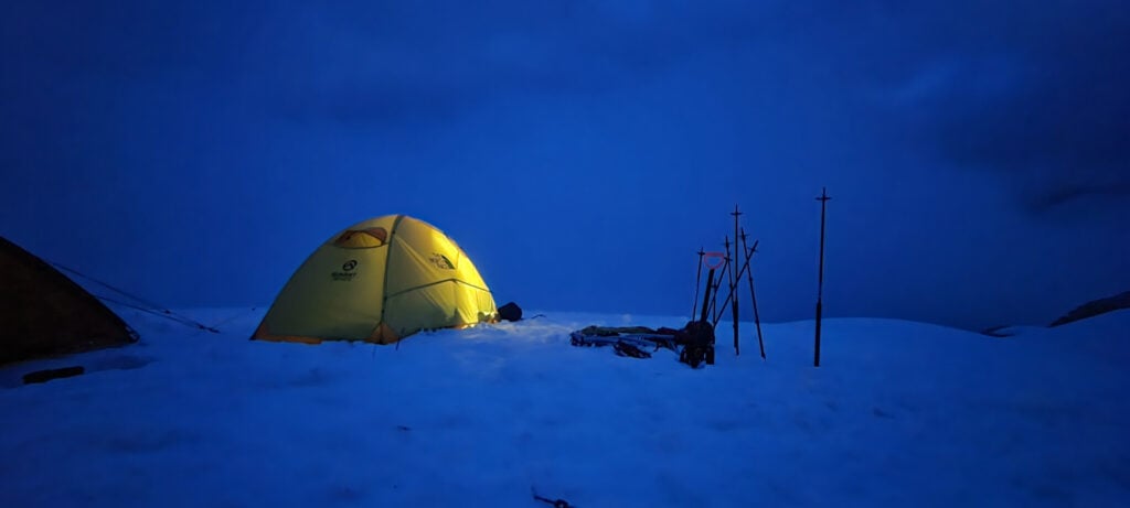 A tent glows in the night in the snow on an American Alpine Institute winter camping course